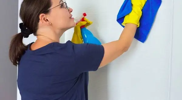 Mujer con guantes amarillos y paño azul limpiando puerta lacada en blanco con spray.