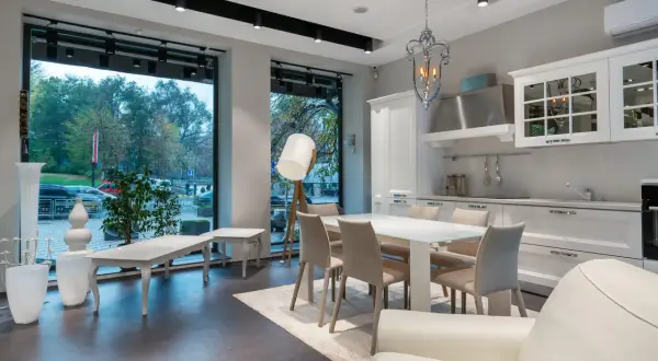 Espaciosa cocina salón comedor de 30 m2 con isla, mesa y sillas, sofá blanco y gran ventanal.