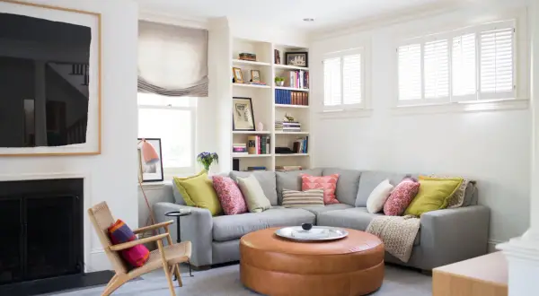 Un salón moderno y acogedor con un sofá rinconera gris, cojines coloridos y un puf de cuero. Ideal para decorar salón con sofá rinconera.