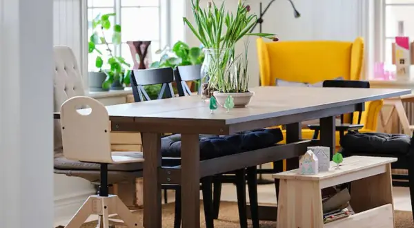 Un banco almacenaje de madera clara, perfecto para guardar libros y objetos, complementa la mesa de comedor.