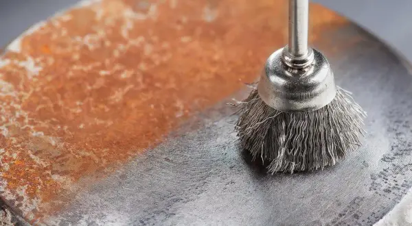 Cepillo metálico eliminando óxido de una superficie. Demuestra cómo quitar el óxido del metal, dejando una zona limpia y brillante.
