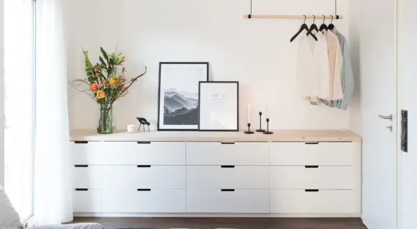 Ideas para decorar cómoda dormitorio matrimonio: ramo de flores, cuadros, velas y ropa colgada.