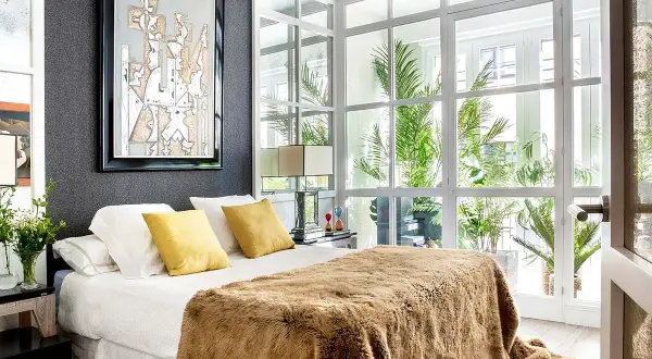 Dormitorio de matrimonio moderno con manta peluda y arte abstracto. Las ultimas tendencias en decoracion de dormitorios de matrimonio se reflejan en la luz natural y las plantas.