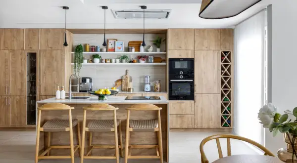 Cocina moderna con armarios de madera clara, isla central con taburetes y estanterías decoradas. Ideal para inspiración de decoracion cocinas.