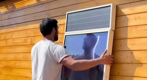 Hombre instala panel solar para calefacción en pared de madera.