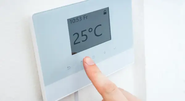 Un dedo ajusta la temperatura en un termostato digital que muestra 25°C.