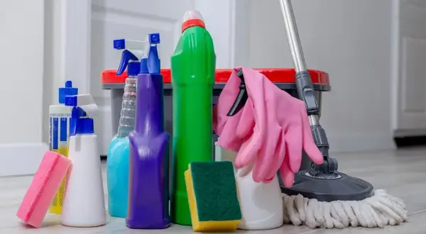 Un surtido de 25 productos de limpieza del hogar, incluyendo botellas rociadoras, esponjas, guantes rosas y un trapeador, listos para dejar tu casa reluciente.