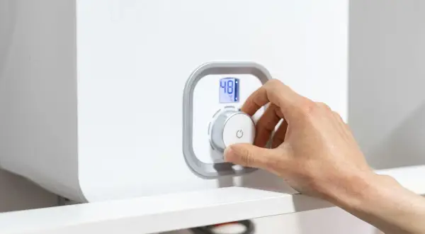 Mano girando el dial de la caldera para subir la presión. La pantalla digital muestra 48°C.