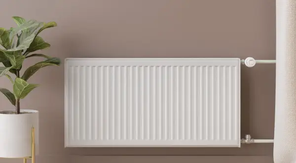 Un radiador blanco, moderno y elegante, calienta la estancia. A su lado, una planta en maceta dorada aporta vida.