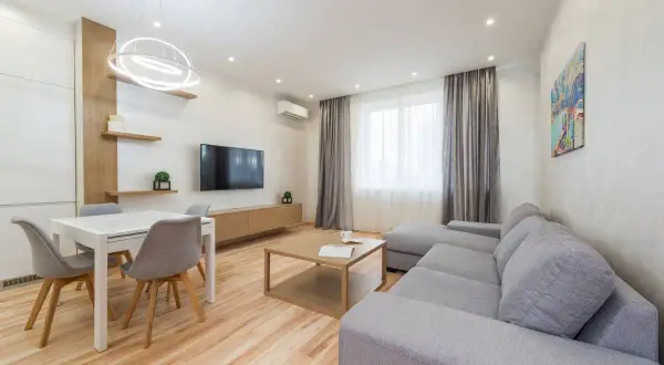Elegante salón con sofá gris, mesa de comedor blanca y detalles en madera. Los colores del salón crean un ambiente acogedor y moderno.