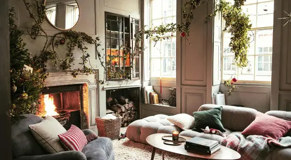 Acogedor salón decorado de Navidad con chimenea encendida, árbol y guirnaldas verdes colgando.