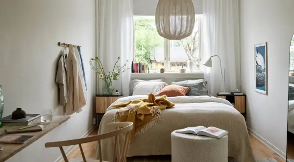 Acogedora cama bajo ventana, con manta amarilla y cojines. Ideas para un dormitorio luminoso y funcional.