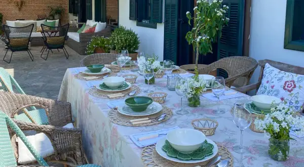 Elegante decoracion mesa cocina al aire libre, con vajilla blanca y verde, flores y asientos de mimbre.