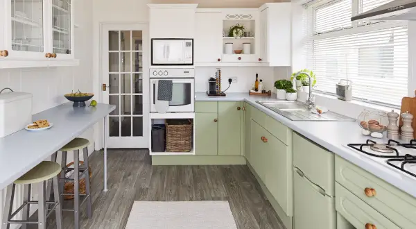 Cocina renovada con gabinetes verdes, encimeras grises y electrodomésticos blancos. Un espacio luminoso y funcional para tu reforma cocina.