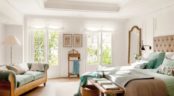 Ideas dormitorio matrimonio: cama con cabecero tapizado, sofá verde, espejo de cuerpo entero y ventanas con luz natural.