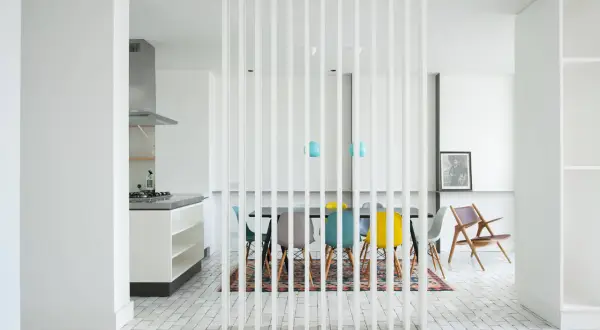 Elegante divisor vertical para dividir salón en dos ambientes, separando la cocina de la zona de comedor con sillas de colores.