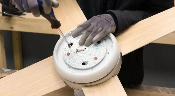 Manos enguantadas atornillan el motor de un ventilador de techo.