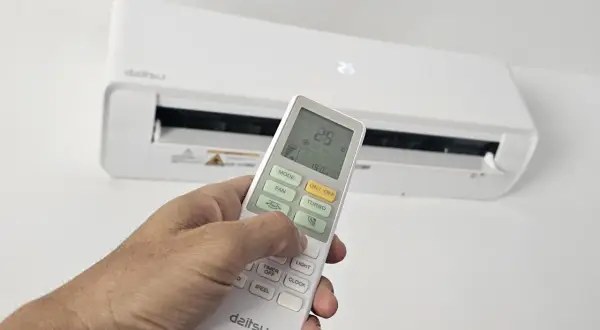 Mano ajustando el control remoto del aire acondicionado para cambiar la temperatura. La pantalla muestra 25.5°C.