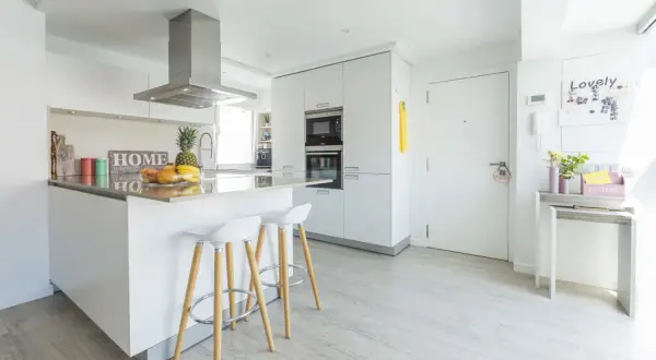 Cocinas modernas blancas con isla central, taburetes y electrodomésticos integrados. Un espacio luminoso y funcional.