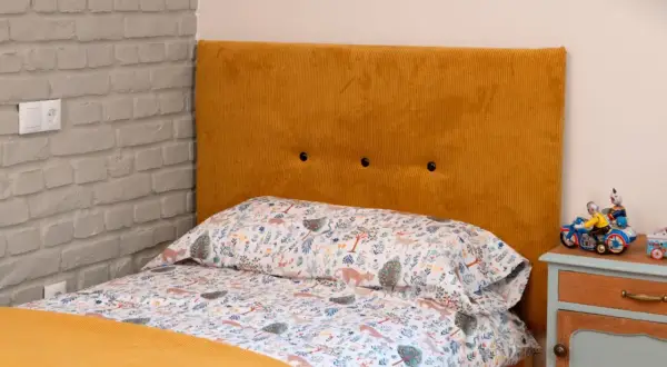 Cabecero tapizado en pana mostaza, ideal para aprender como tapizar un cabecero. Cama con ropa de cama infantil y mesita de noche.