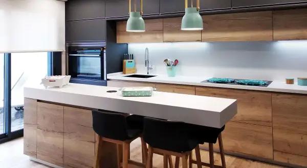 Cocina moderna con isla y taburetes. Ideas cocinas pequeñas: gabinetes de madera, encimera blanca y detalles en verde menta.