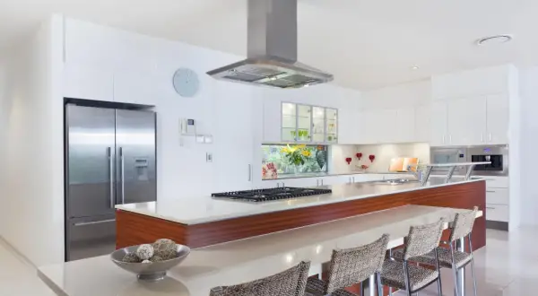 Cocina moderna con isla, nevera de acero inoxidable y campana extractora. Ideal para tu reforma cocina precio.