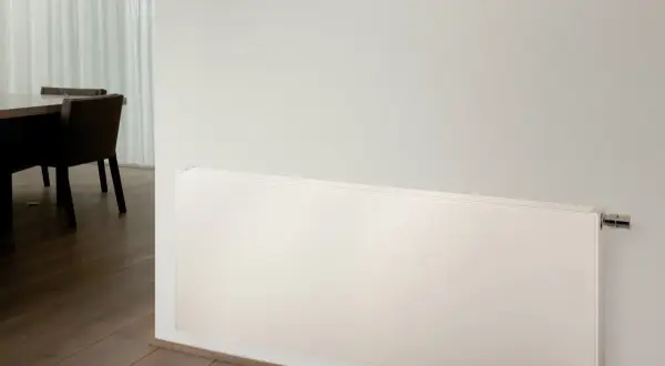 Radiadores de alta temperatura blancos, modernos y discretos, instalados en una pared junto a un suelo de madera y una mesa con sillas.