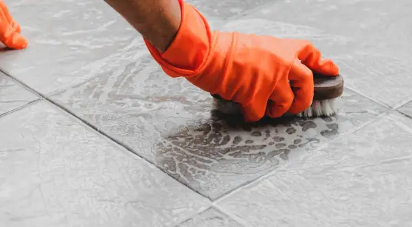 Mano con guante naranja cepillando suelo de terrazo con espuma. Limpiar suelo de terrazo es fácil con esta técnica.