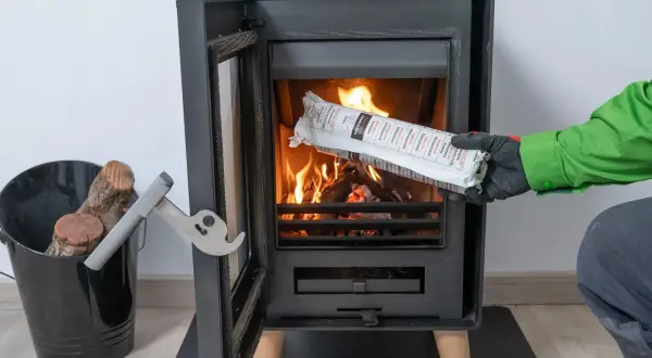 Persona con guantes verdes y grises introduce un producto envasado en una chimenea encendida. Es parte de la limpieza de chimeneas.