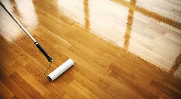 Rodillo aplicando barniz a un suelo de parquet de madera, restaurando su brillo. Mantenimiento parquet.
