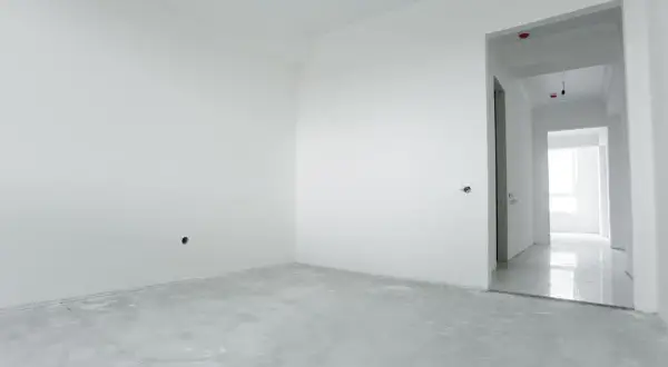 Habitación vacía con paredes blancas y suelo de cemento. El yeso aguanta el calor, preparándose para un nuevo hogar.