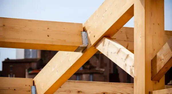 Estructura de vigas de madera clara, parte de techos de madera en construcción, con uniones metálicas visibles.