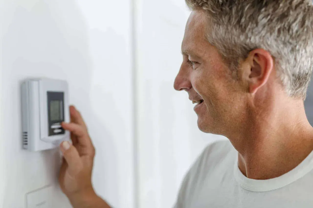 Hombre ajustando el termostato para entender como funciona un termostato de calefacción y mantener la temperatura ideal en casa.