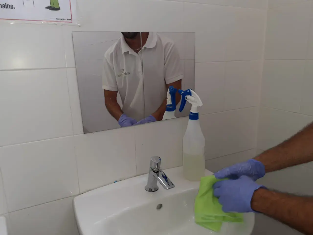 Man con guantes limpia lavabo con paño verde. Spray de limpieza cerca. Aprende como limpiar azulejos baño.