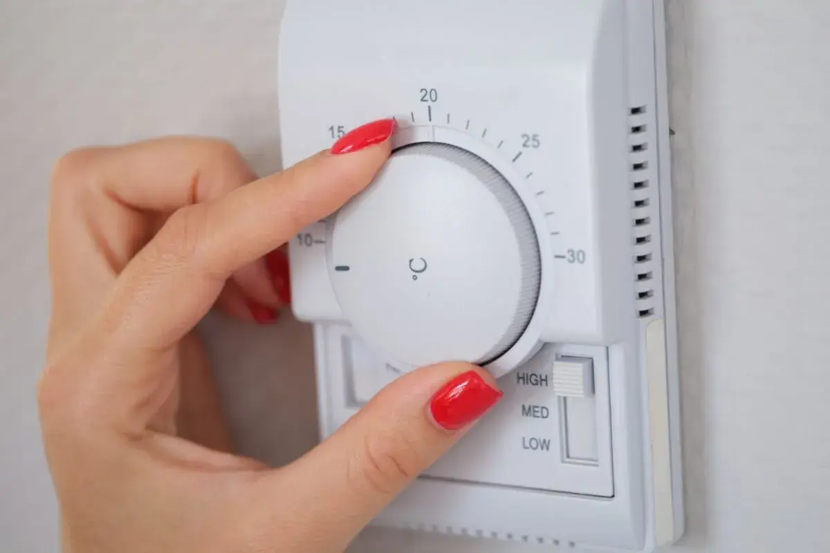 Mano ajustando el termostato para saber como poner la calefacción en casa. La temperatura se marca en grados Celsius.
