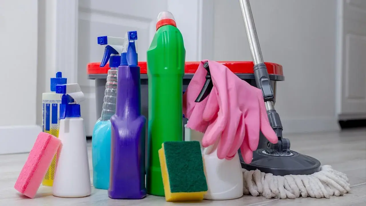 Un surtido de 25 productos de limpieza del hogar, incluyendo botellas rociadoras, esponjas, guantes rosas y un trapeador, listos para dejar tu casa reluciente.