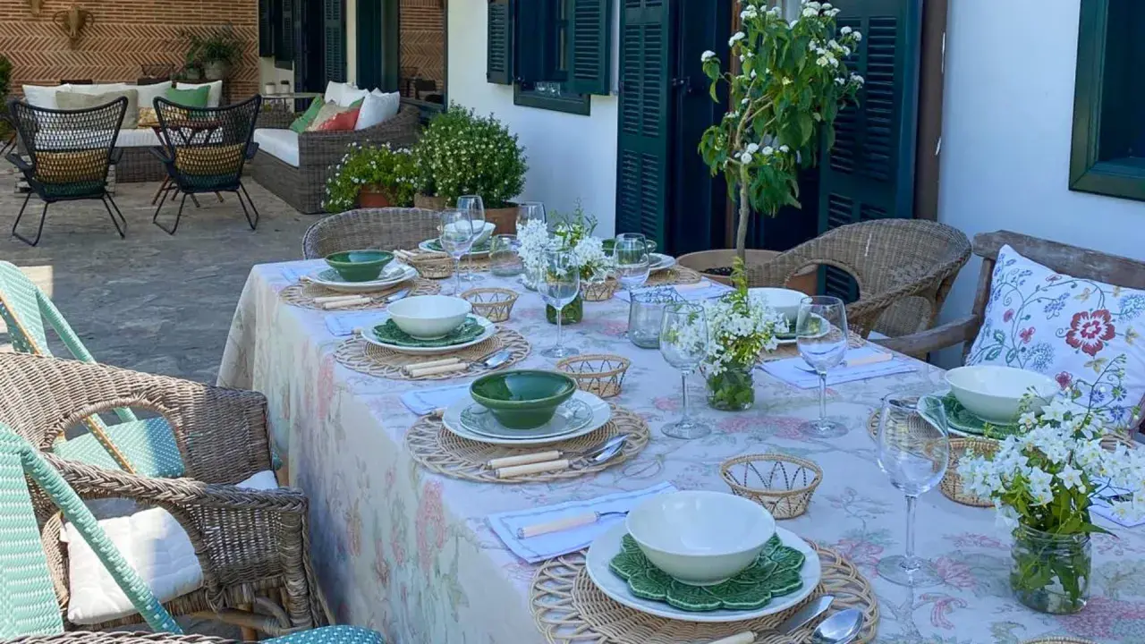 Elegante decoracion mesa cocina al aire libre, con vajilla blanca y verde, flores y asientos de mimbre.