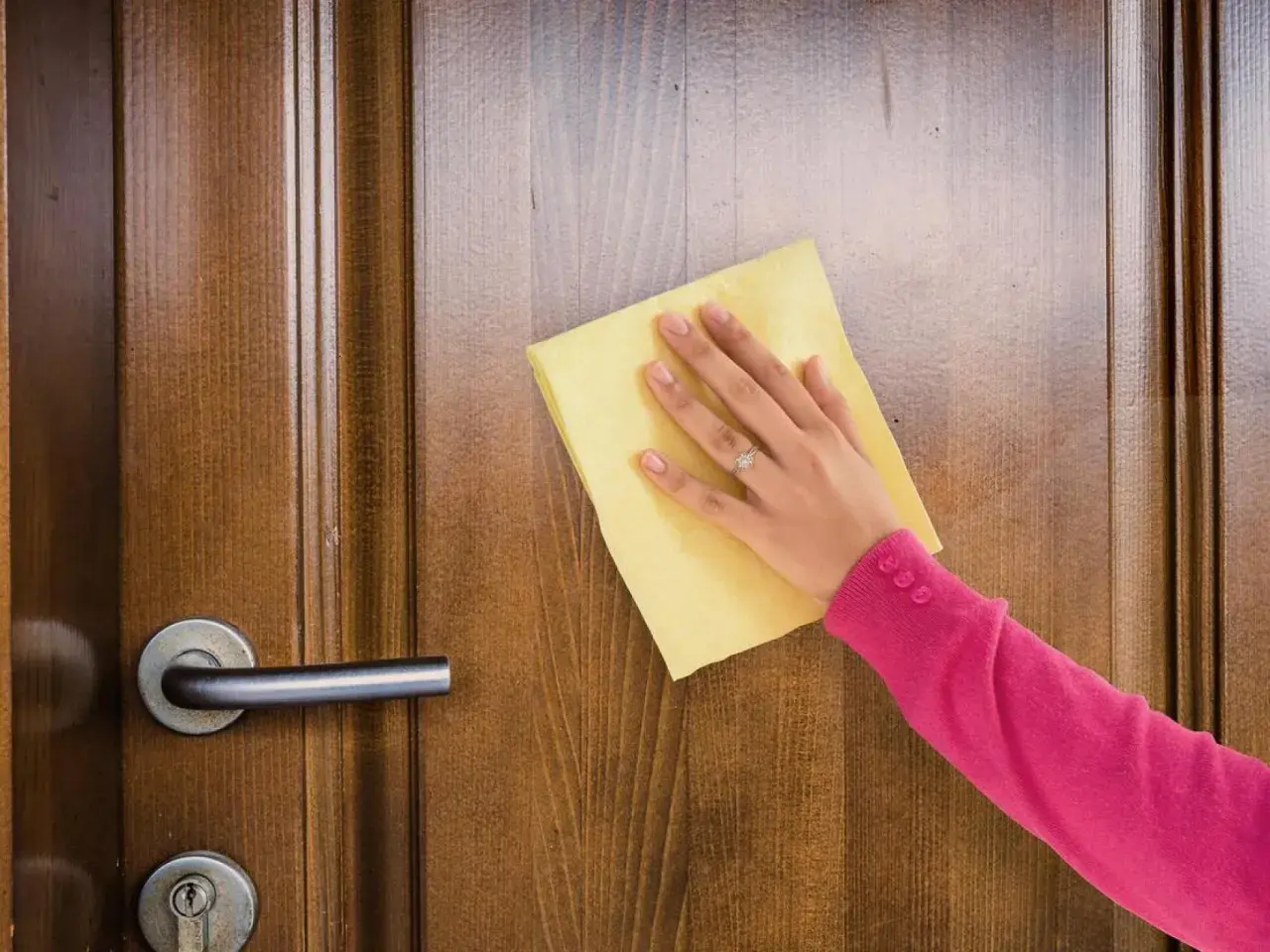 Mano con paño amarillo limpiando puertas de madera barnizadas muy sucias.