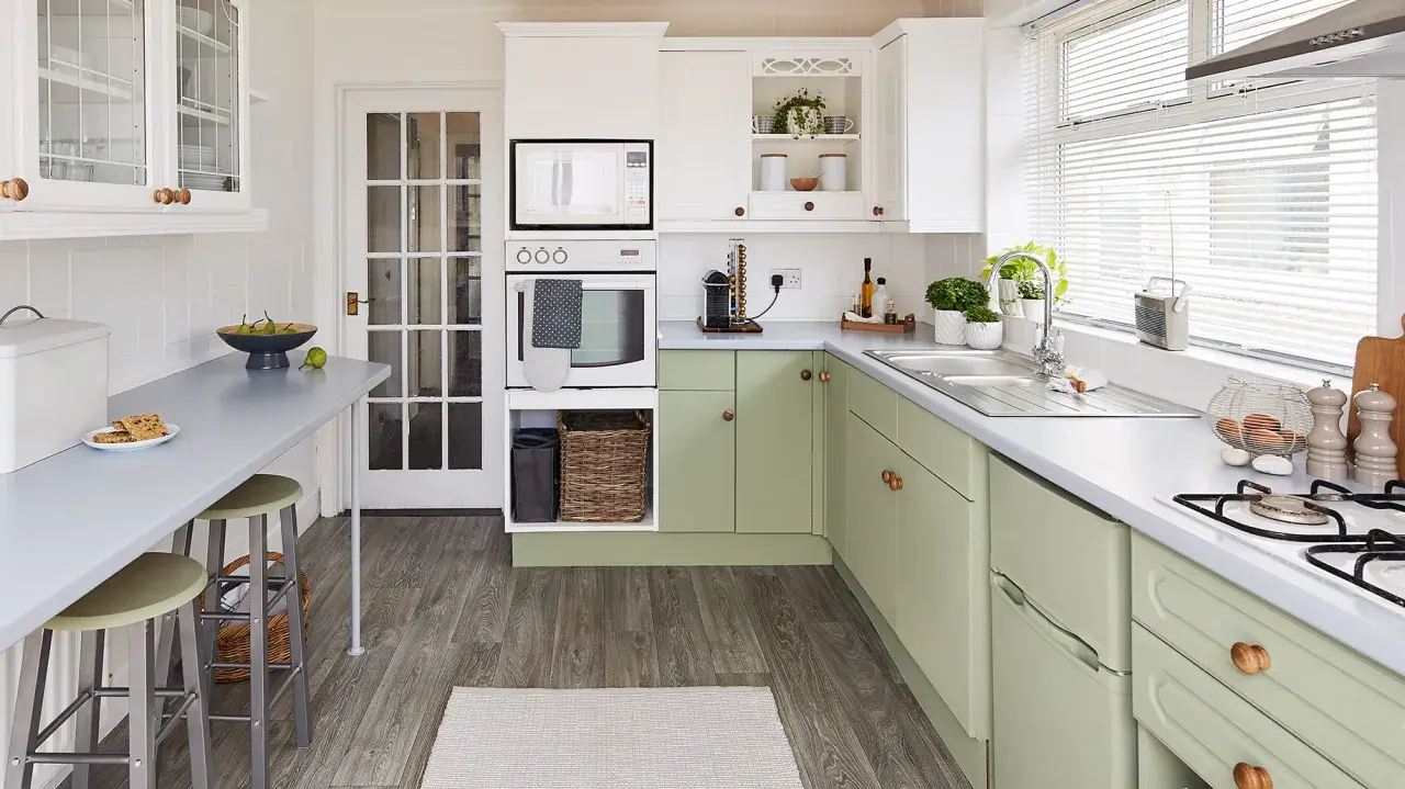 Cocina renovada con gabinetes verdes, encimeras grises y electrodomésticos blancos. Un espacio luminoso y funcional para tu reforma cocina.