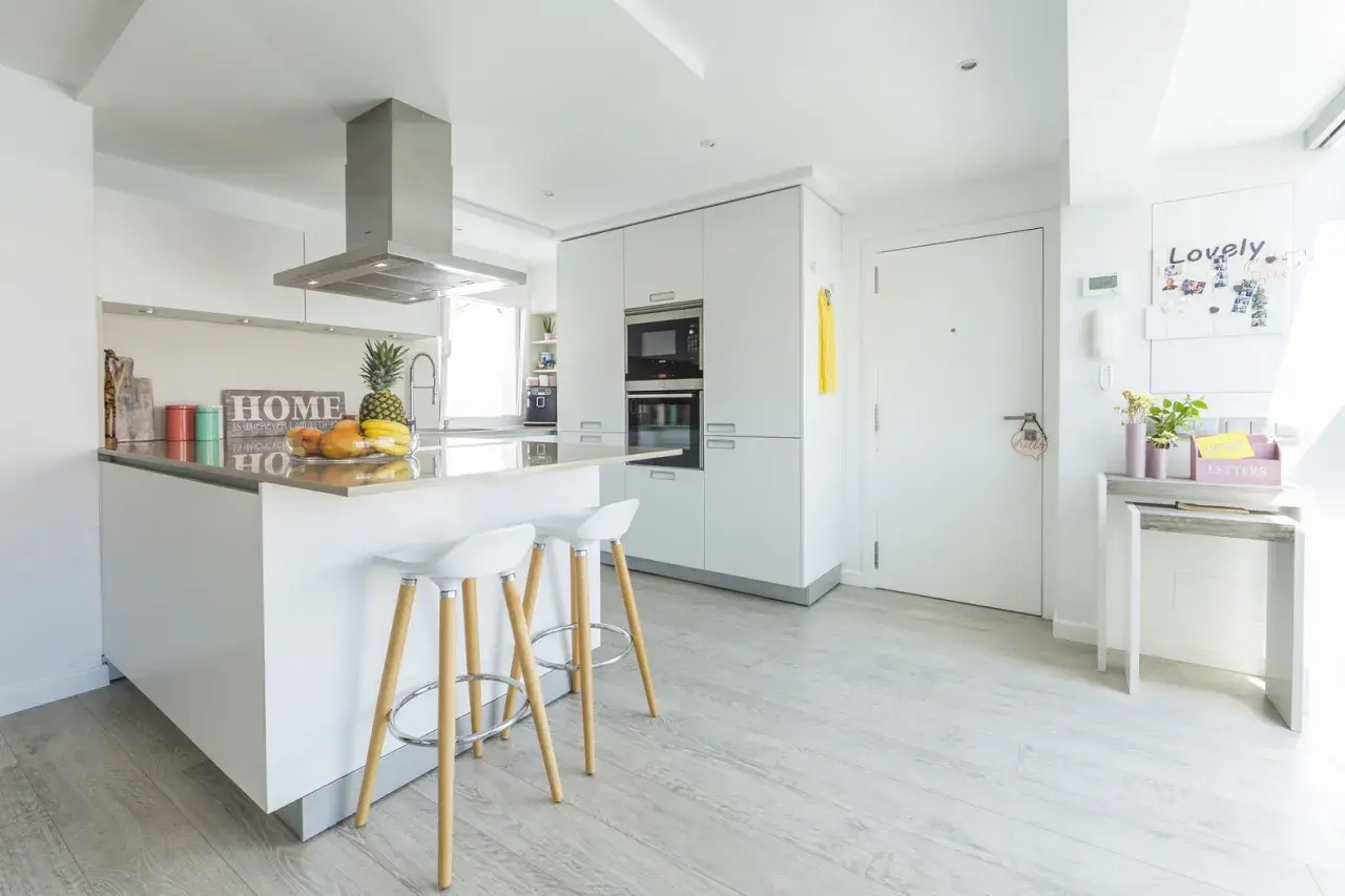 Cocinas modernas blancas con isla central, taburetes y electrodomésticos integrados. Un espacio luminoso y funcional.