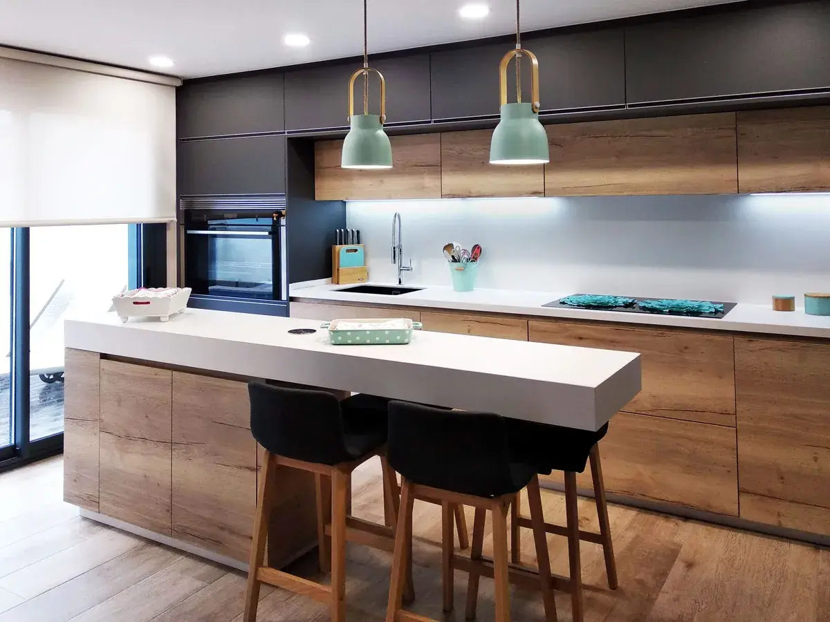Cocina moderna con isla y taburetes. Ideas cocinas pequeñas: gabinetes de madera, encimera blanca y detalles en verde menta.