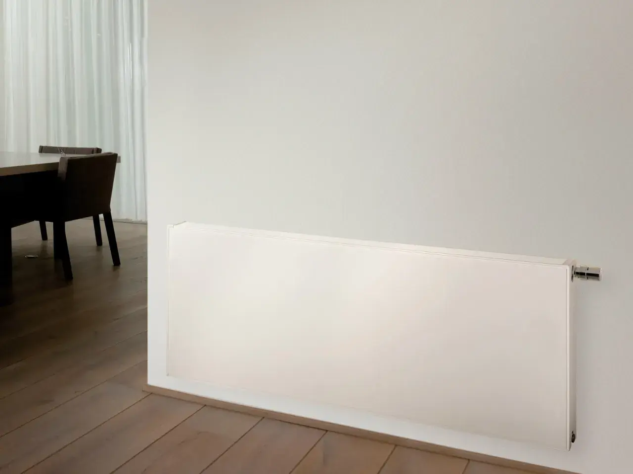 Radiadores de alta temperatura blancos, modernos y discretos, instalados en una pared junto a un suelo de madera y una mesa con sillas.