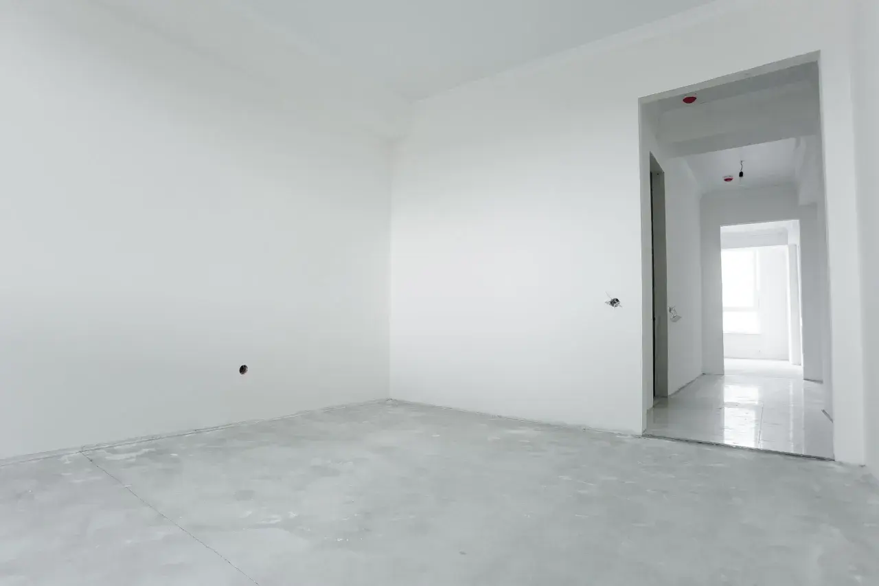 Habitación vacía con paredes blancas y suelo de cemento. El yeso aguanta el calor, preparándose para un nuevo hogar.