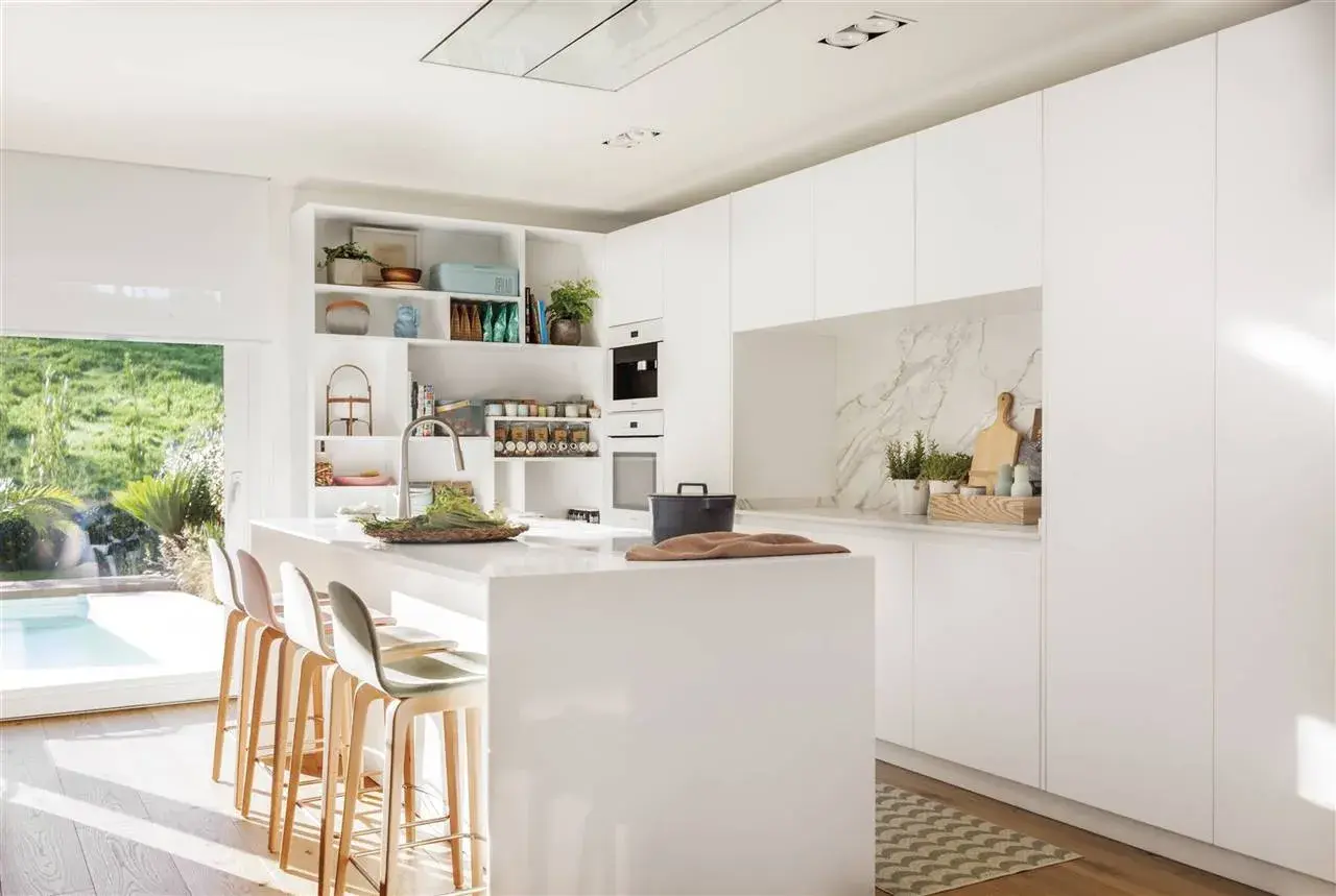 Cocina moderna y luminosa con isla central, taburetes y estanterías. Ideas de diseño cocina minimalista y funcional.