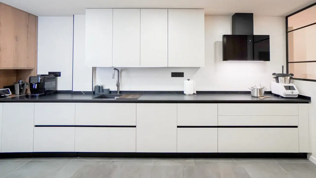 Cocinas modernas blancas con encimera oscura, campana extractora negra y electrodomésticos.