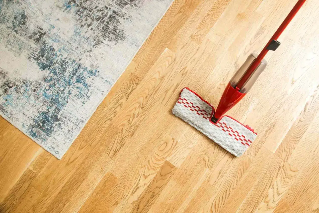 Mopa roja limpiando un suelo de parquet de madera clara, junto a una alfombra con diseño abstracto. Cuidado y mantenimiento del parquet.