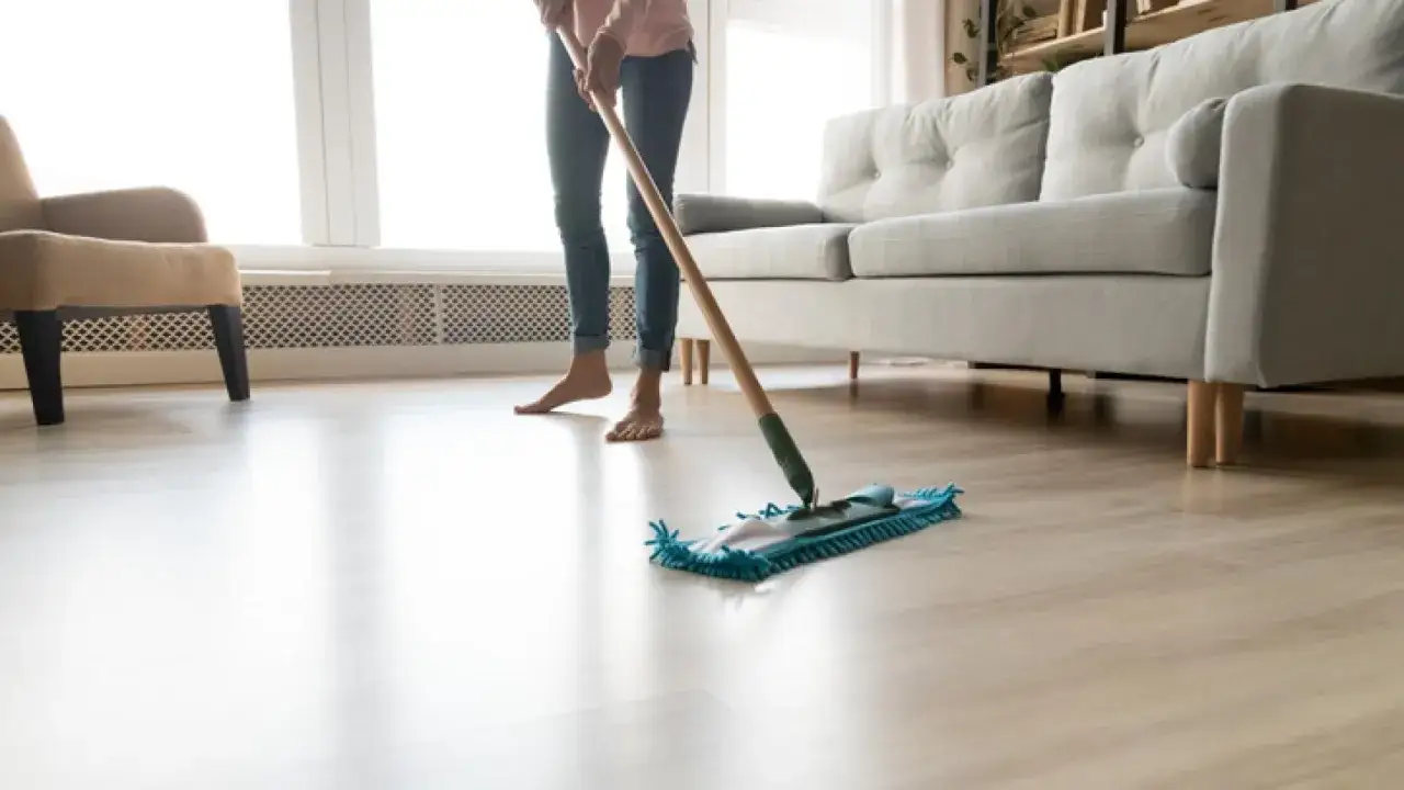 Persona limpiando el suelo de madera con una mopa, dejando un brillo impecable en el salón.