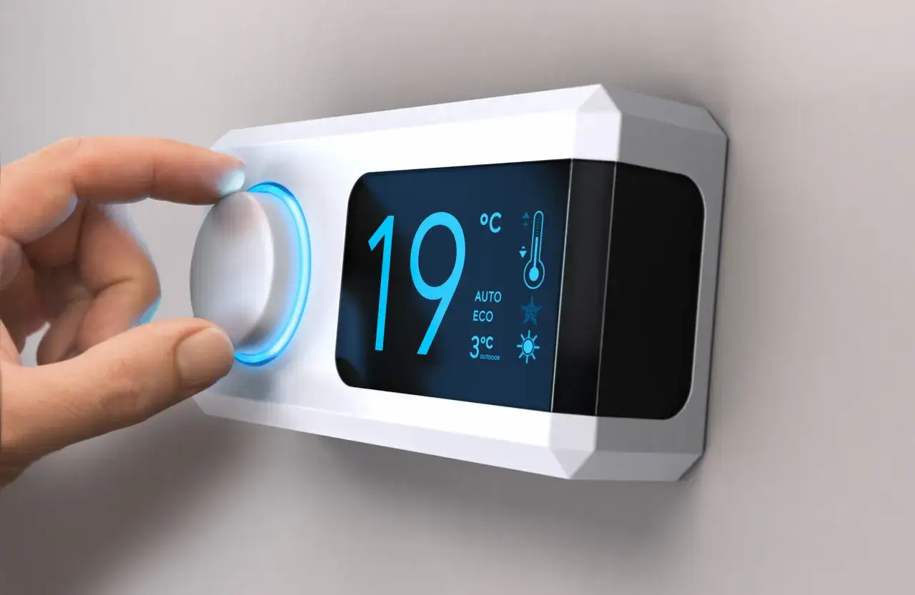 Dedo ajustando el dial de un termostato moderno. La pantalla muestra 19°C, AUTO, ECO y 3°C exterior, indicando una calefacción inteligente.