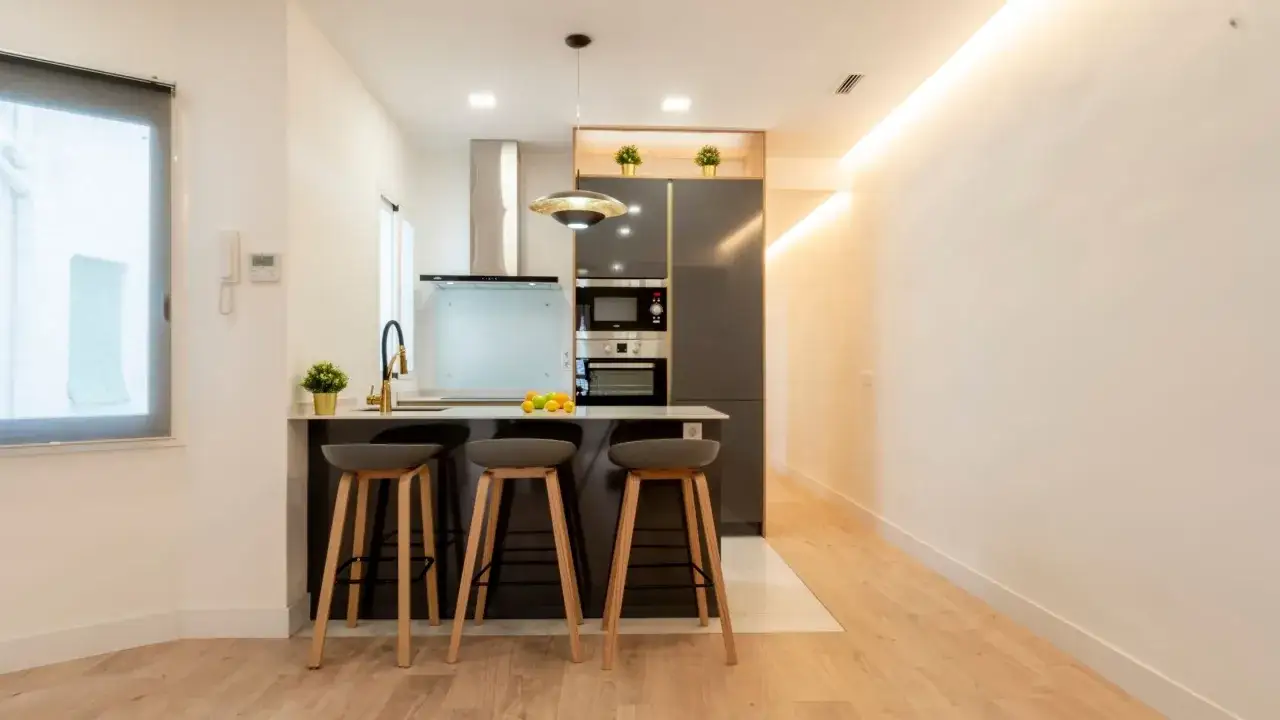 Cocina moderna con isla y taburetes, ideal para ideas cocinas pequeñas. Electrodomésticos integrados y grifería dorada.