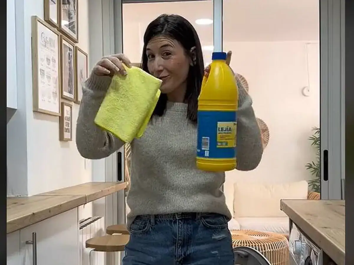 Mujer sonriente con un paño amarillo y una botella de lejía, lista para limpiar la lavadora.